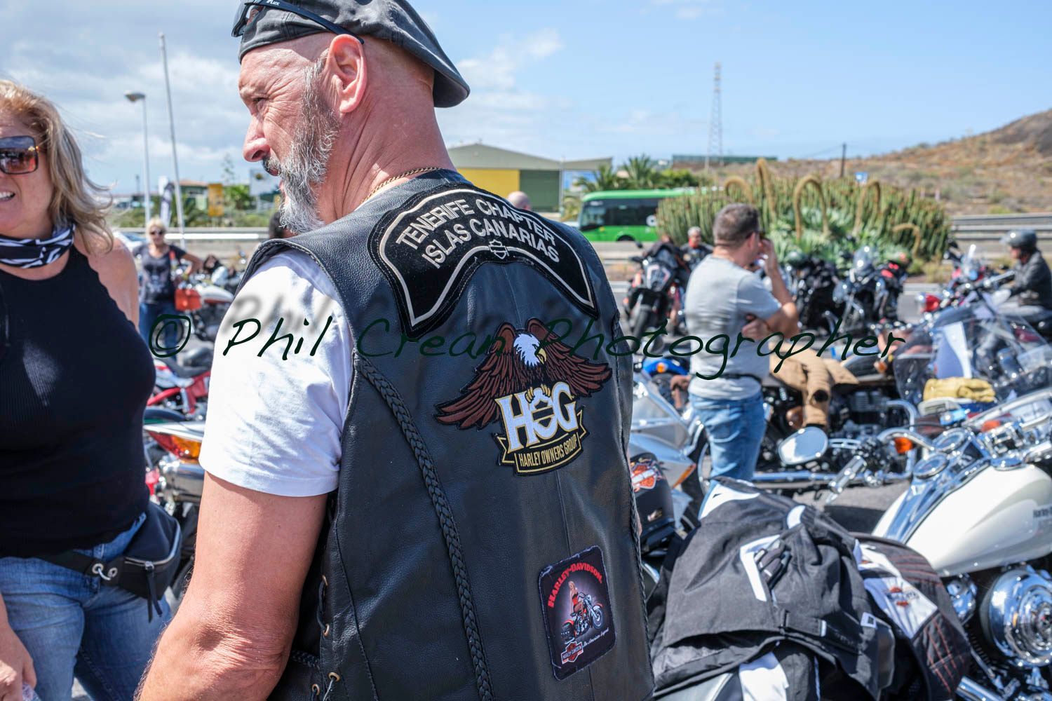 A man wearing a leather vest with the word hog on it is standing in front of a motorcycle.