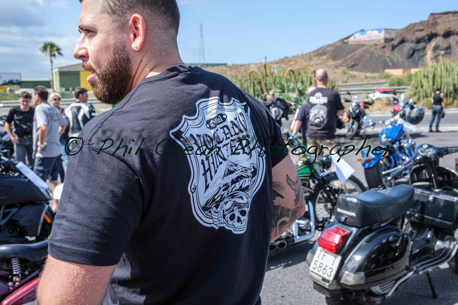 A man with a tattoo on his back is standing in front of motorcycles.