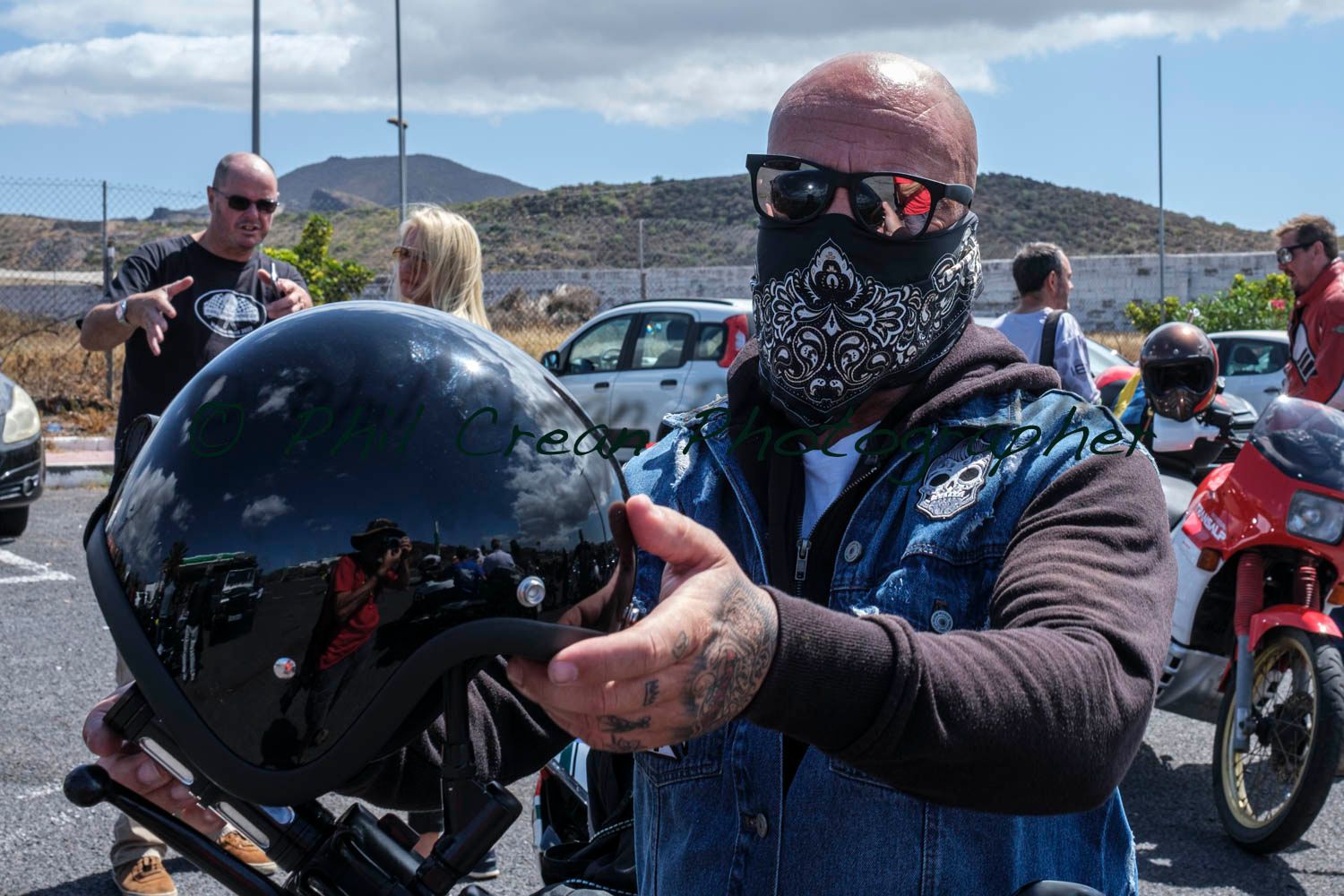 A man wearing a bandana and sunglasses is holding a helmet.
