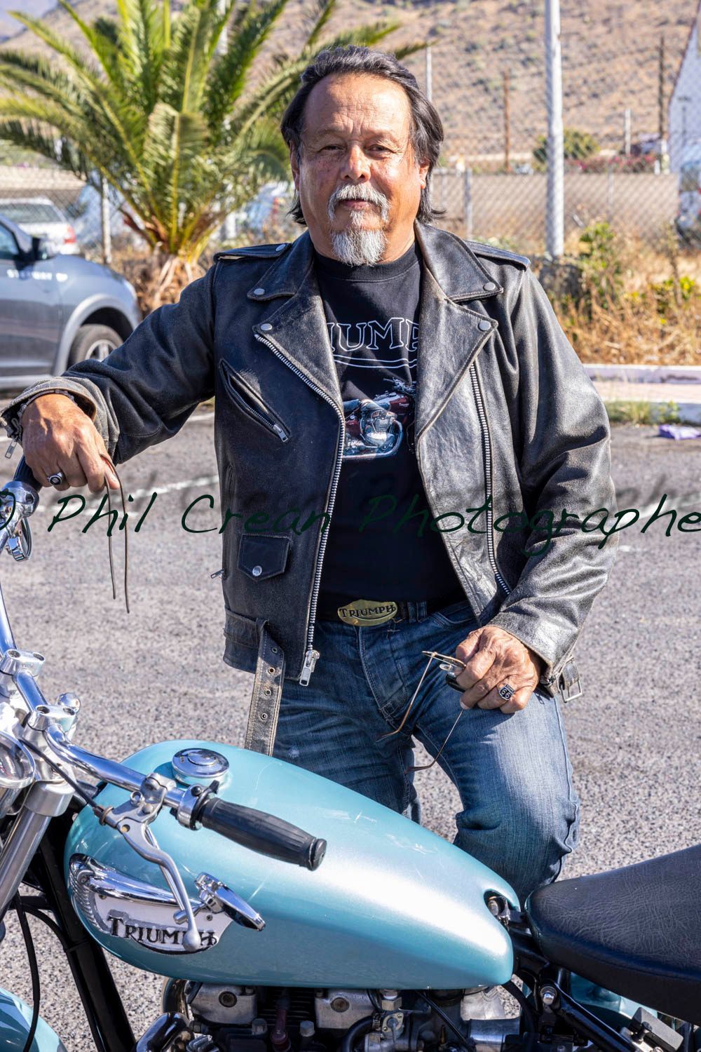 A man in a leather jacket is sitting on a blue motorcycle.