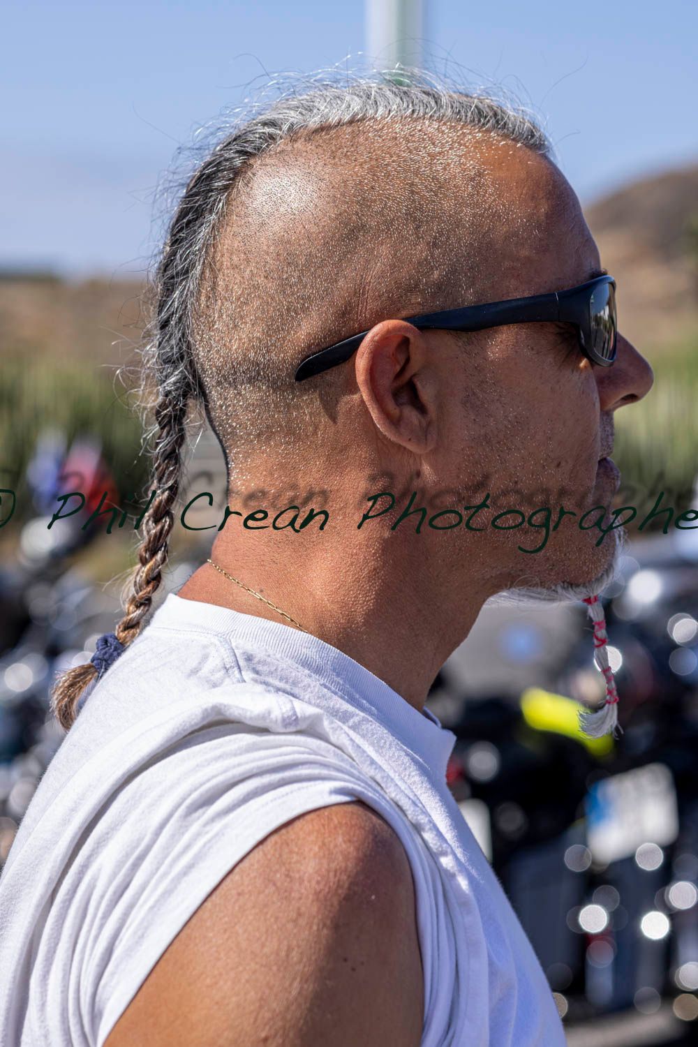 A man with a mohawk and sunglasses is standing in front of motorcycles.