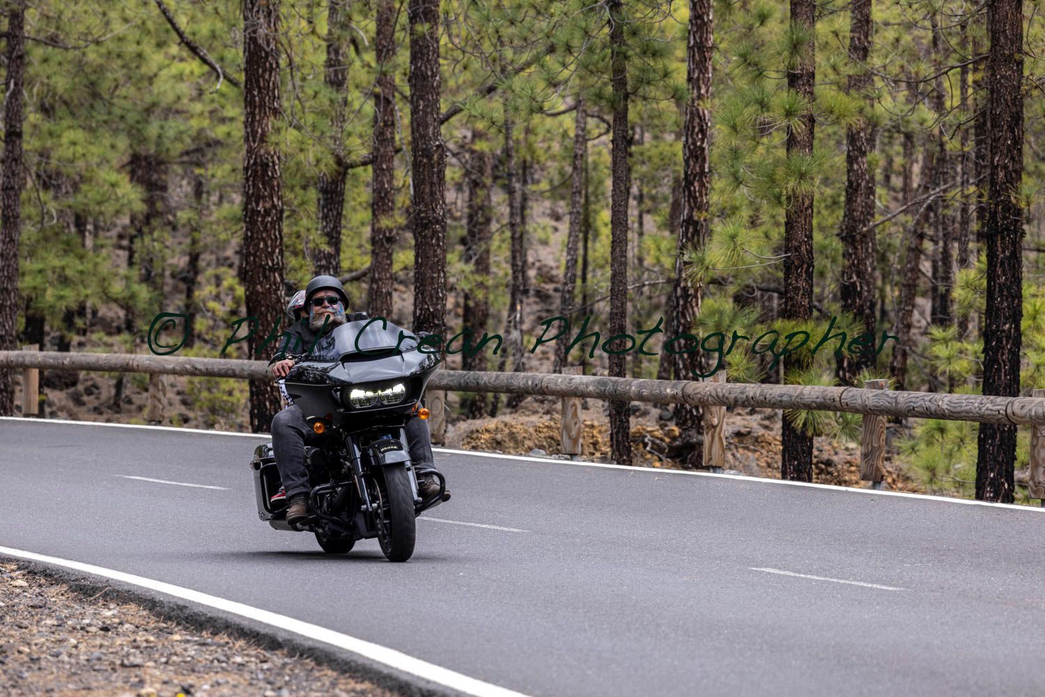A man is riding a motorcycle down a road in the woods.