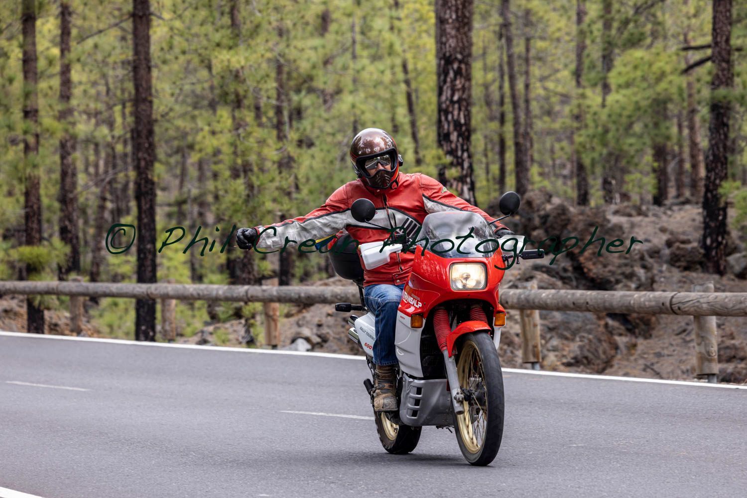 A man is riding a red motorcycle down a road.