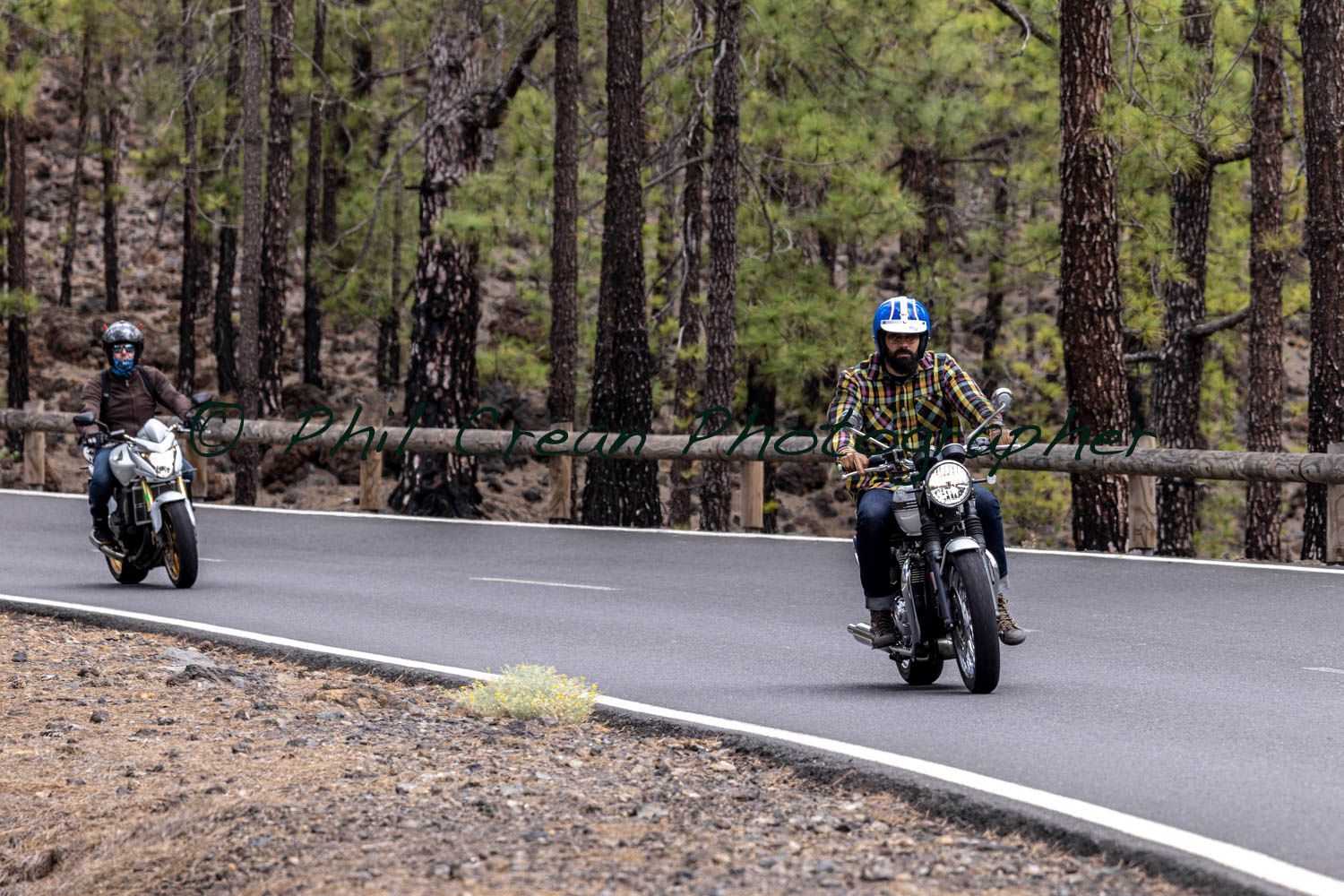 Two people are riding motorcycles down a road in the woods