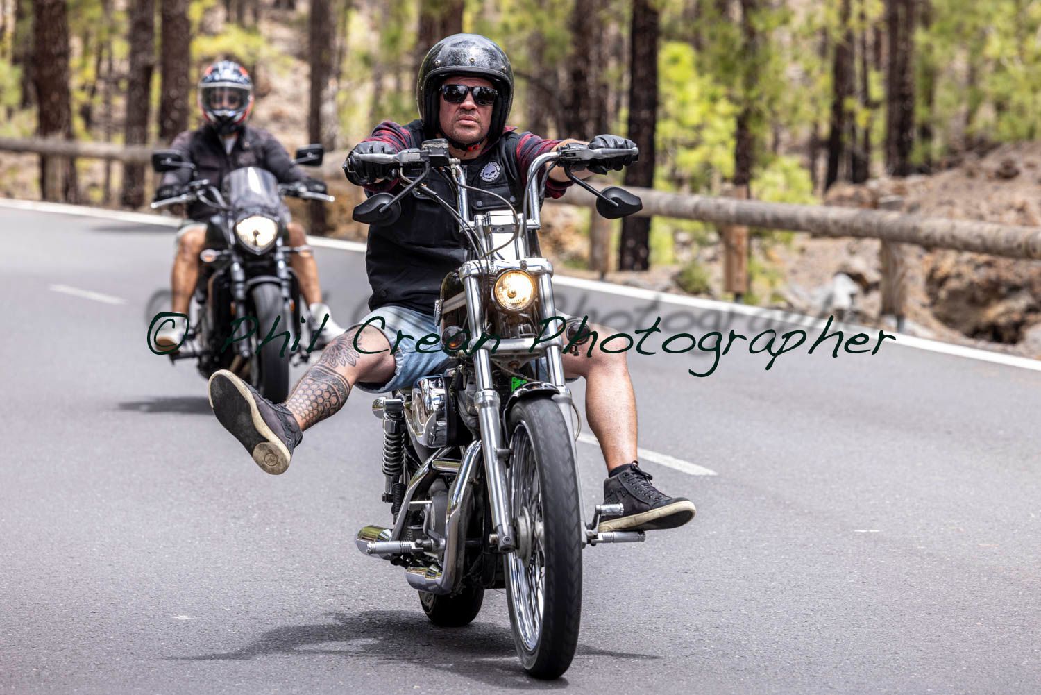 Two men are riding motorcycles down a road.