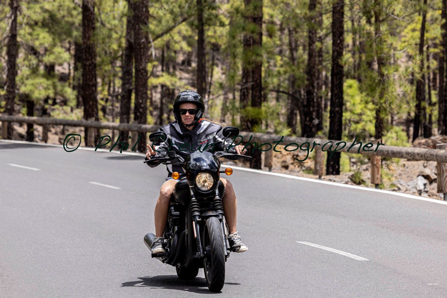 A man is riding a motorcycle down a road surrounded by trees.