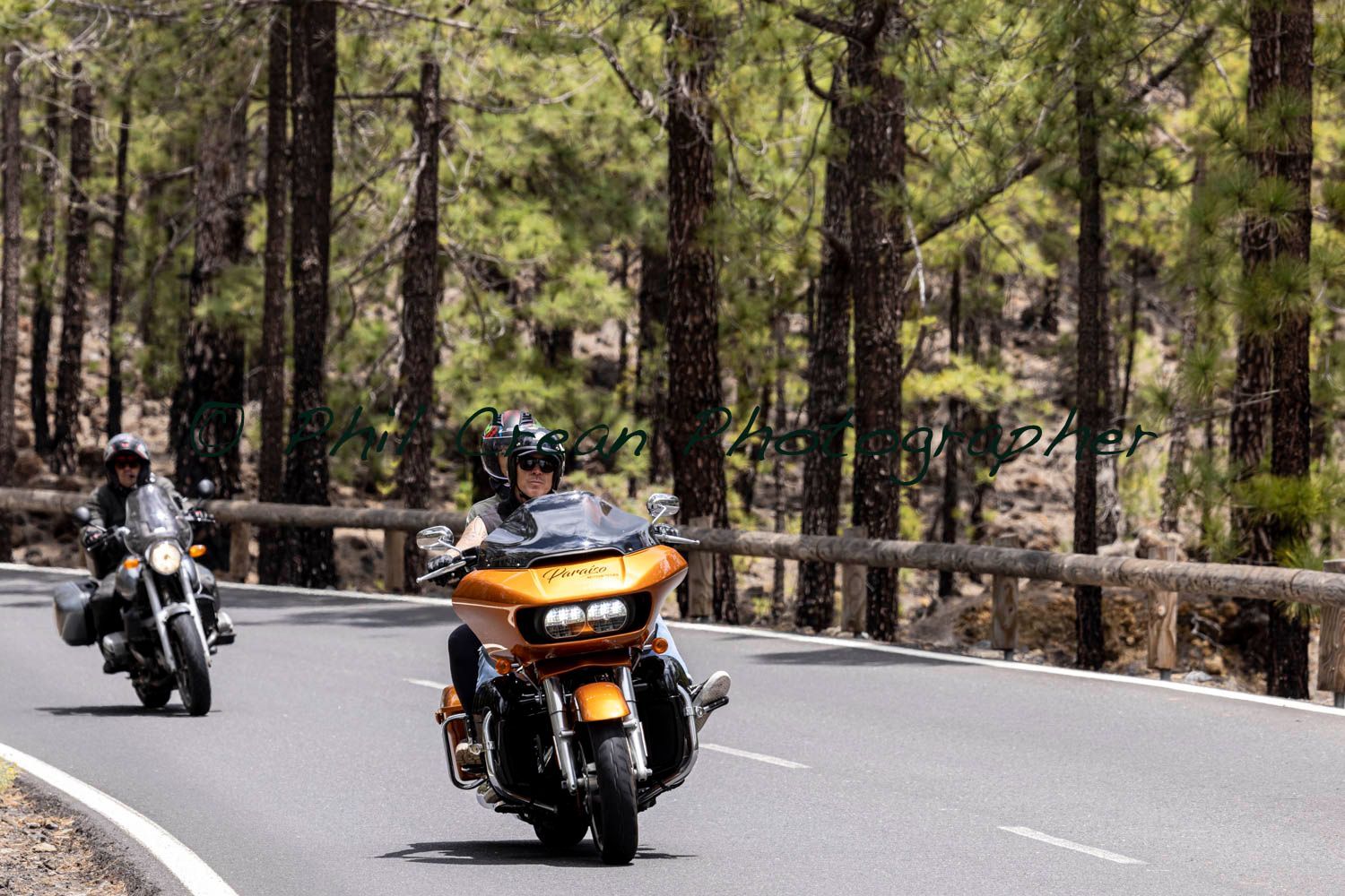 Two people are riding motorcycles down a road in the woods.