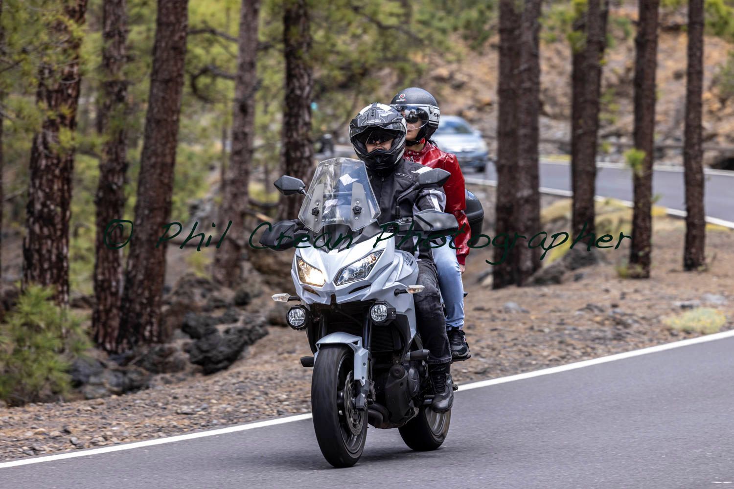 Two people are riding a motorcycle down a road.