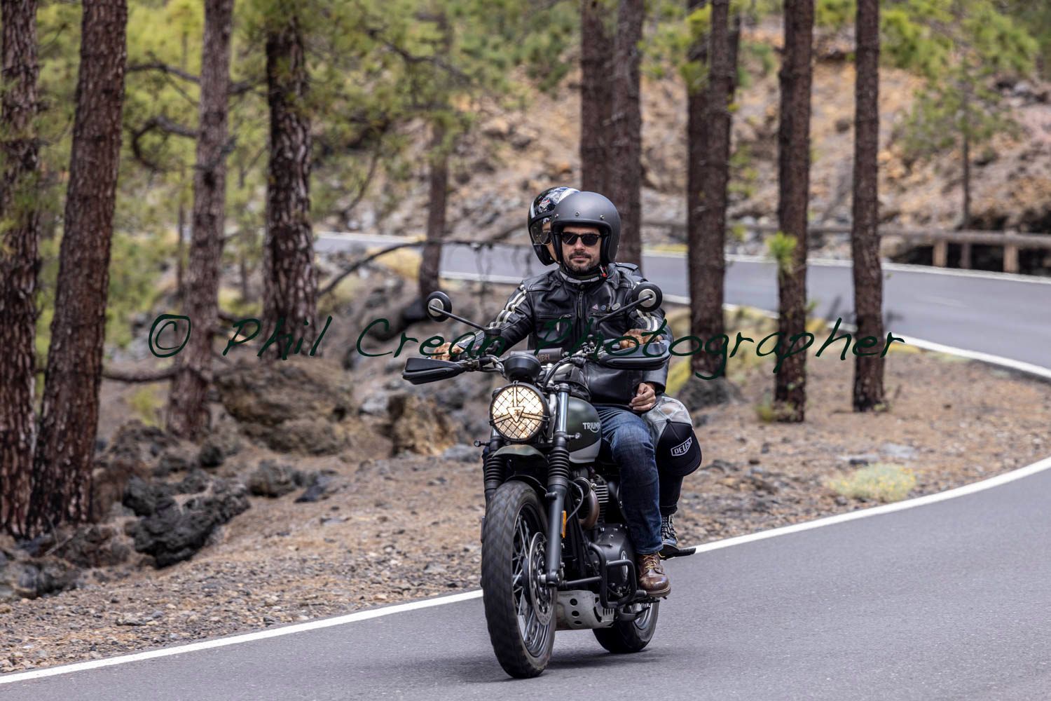 A man is riding a motorcycle down a road in the woods.