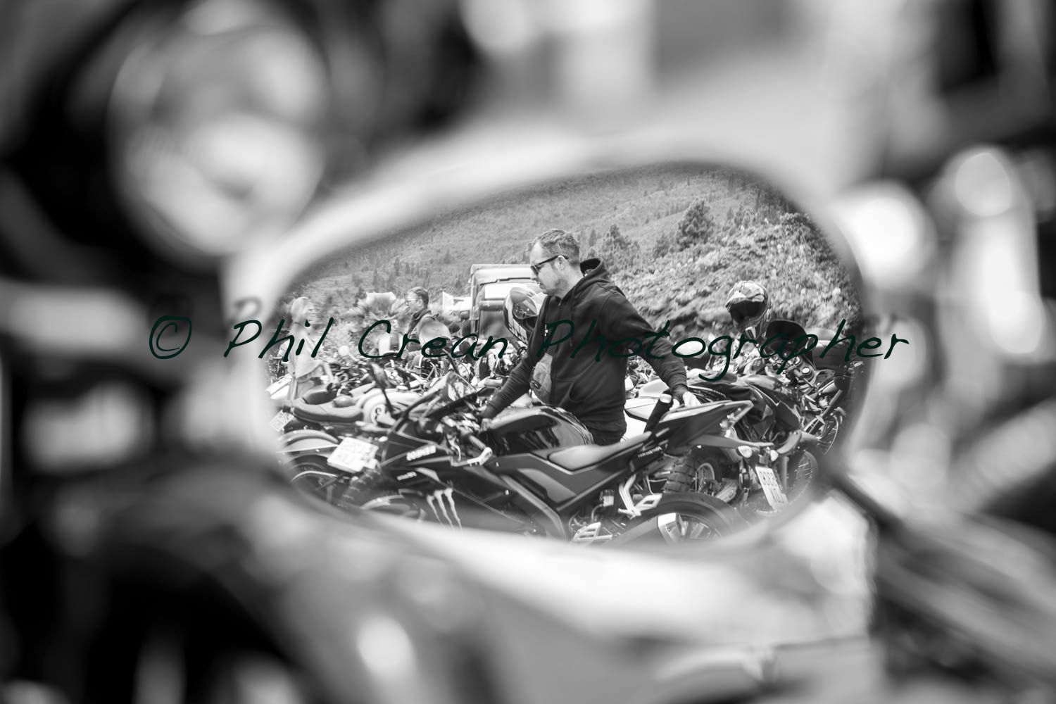 A black and white photo of a person riding a motorcycle in a rear view mirror.