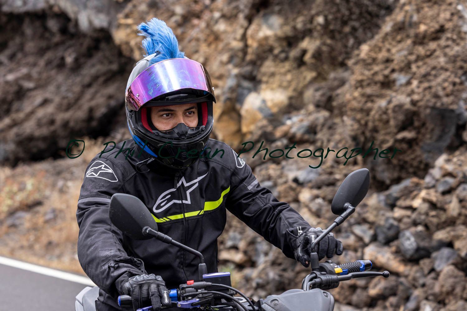 A man wearing a helmet and goggles is riding a motorcycle down a road.