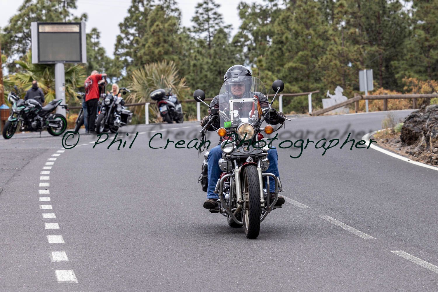 A man is riding a motorcycle down a road with trees in the background