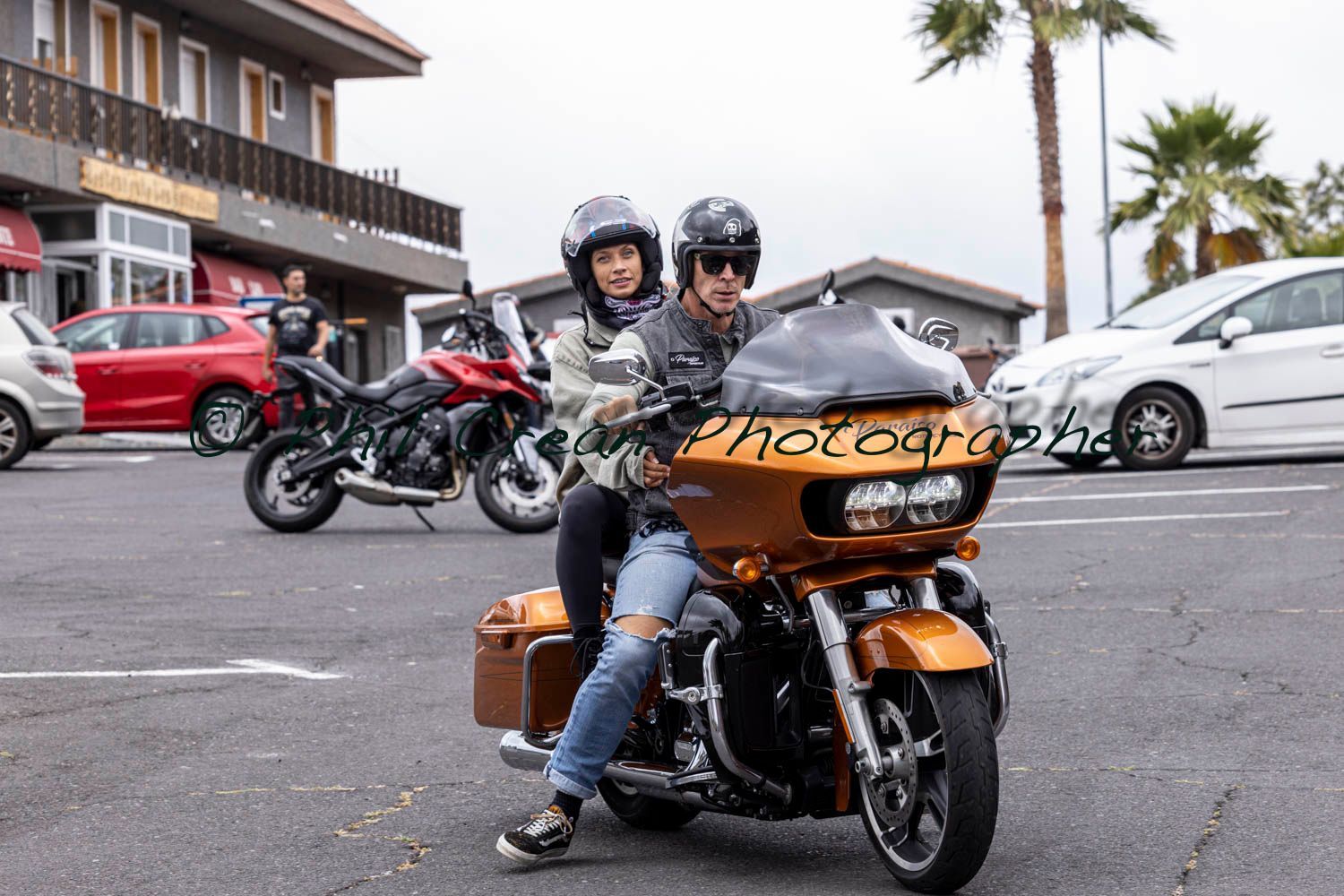 A man and a woman are riding a motorcycle in a parking lot.