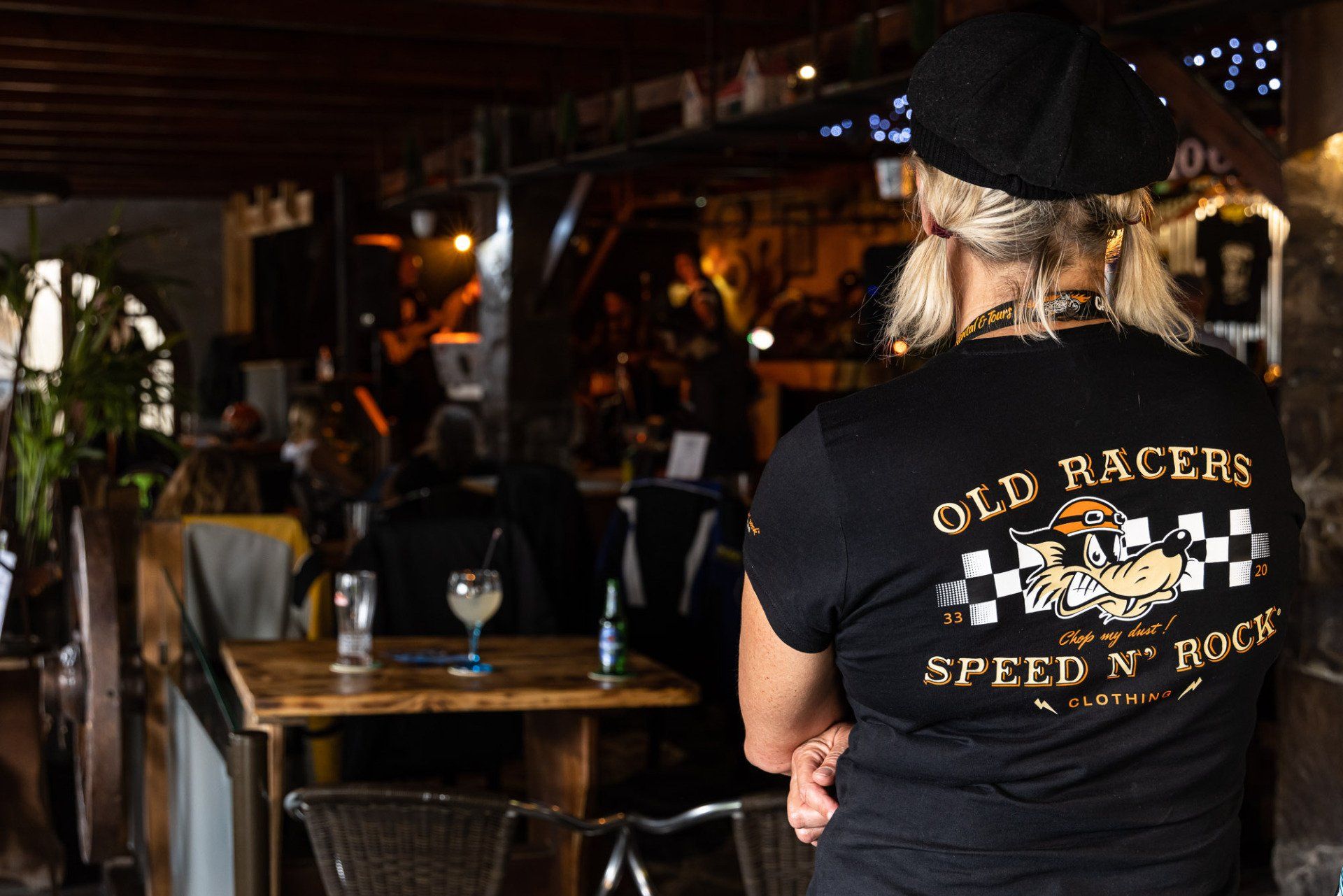 A woman wearing an old racers shirt is standing in a restaurant.