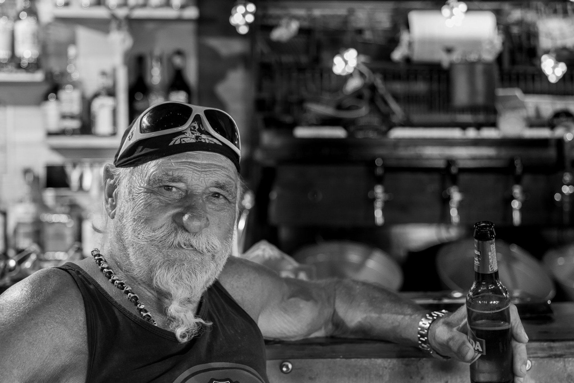 A man with a beard is sitting at a bar holding a bottle of beer.