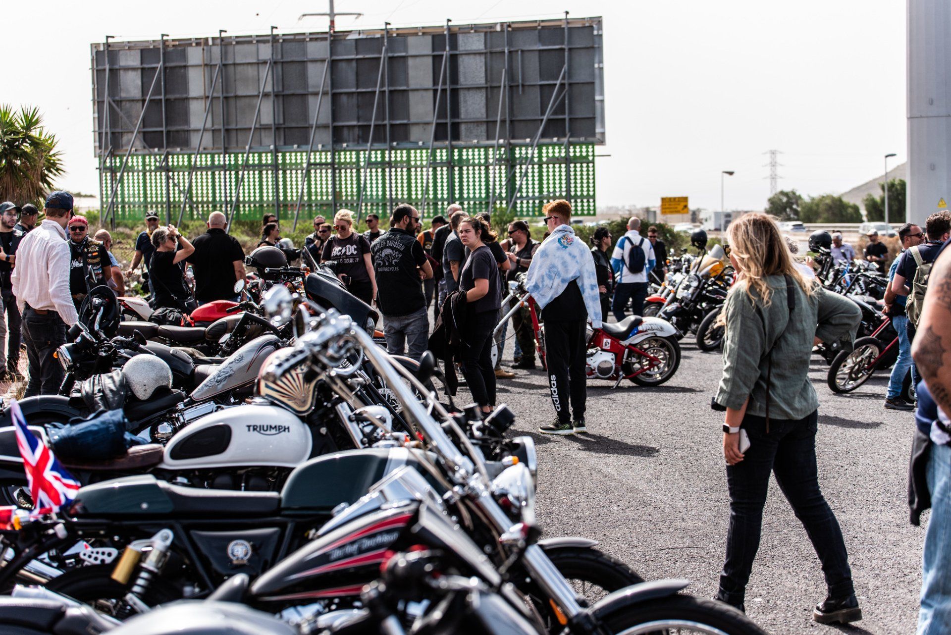 A group of people are standing around motorcycles in a parking lot.
