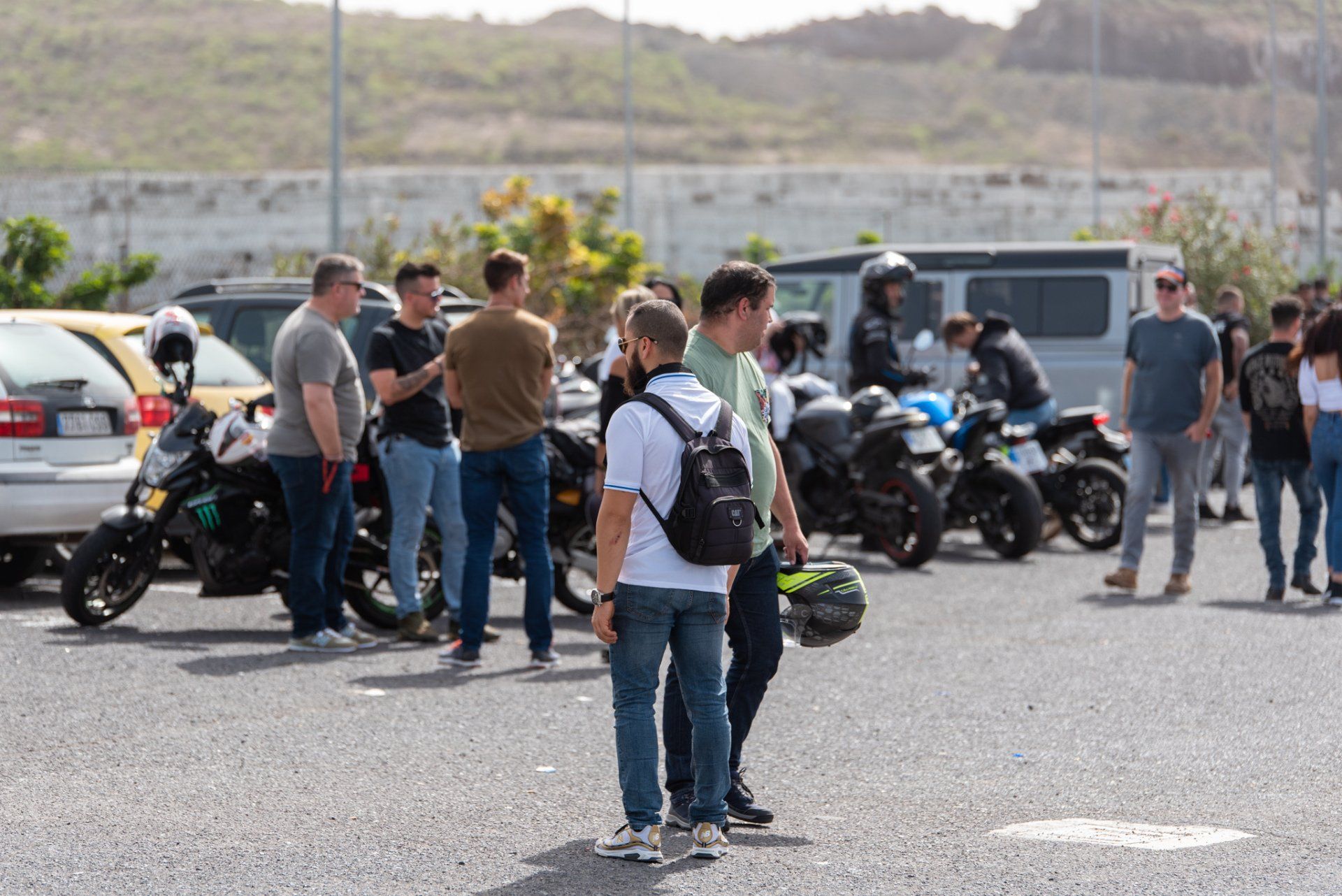A group of people are standing in a parking lot with motorcycles.