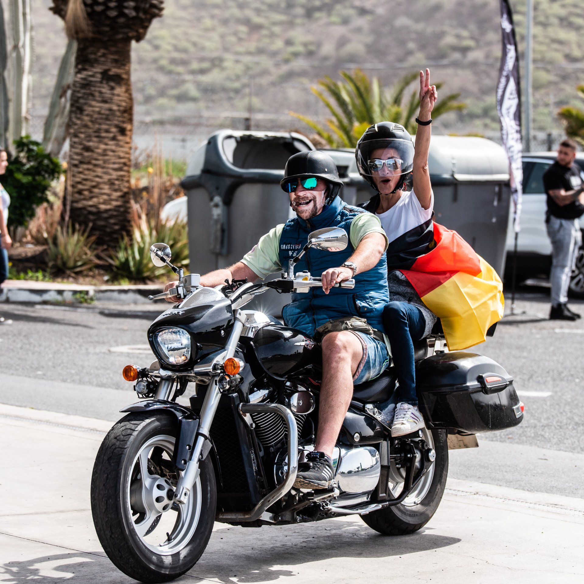 A man and a woman are riding a motorcycle with a german flag on the back