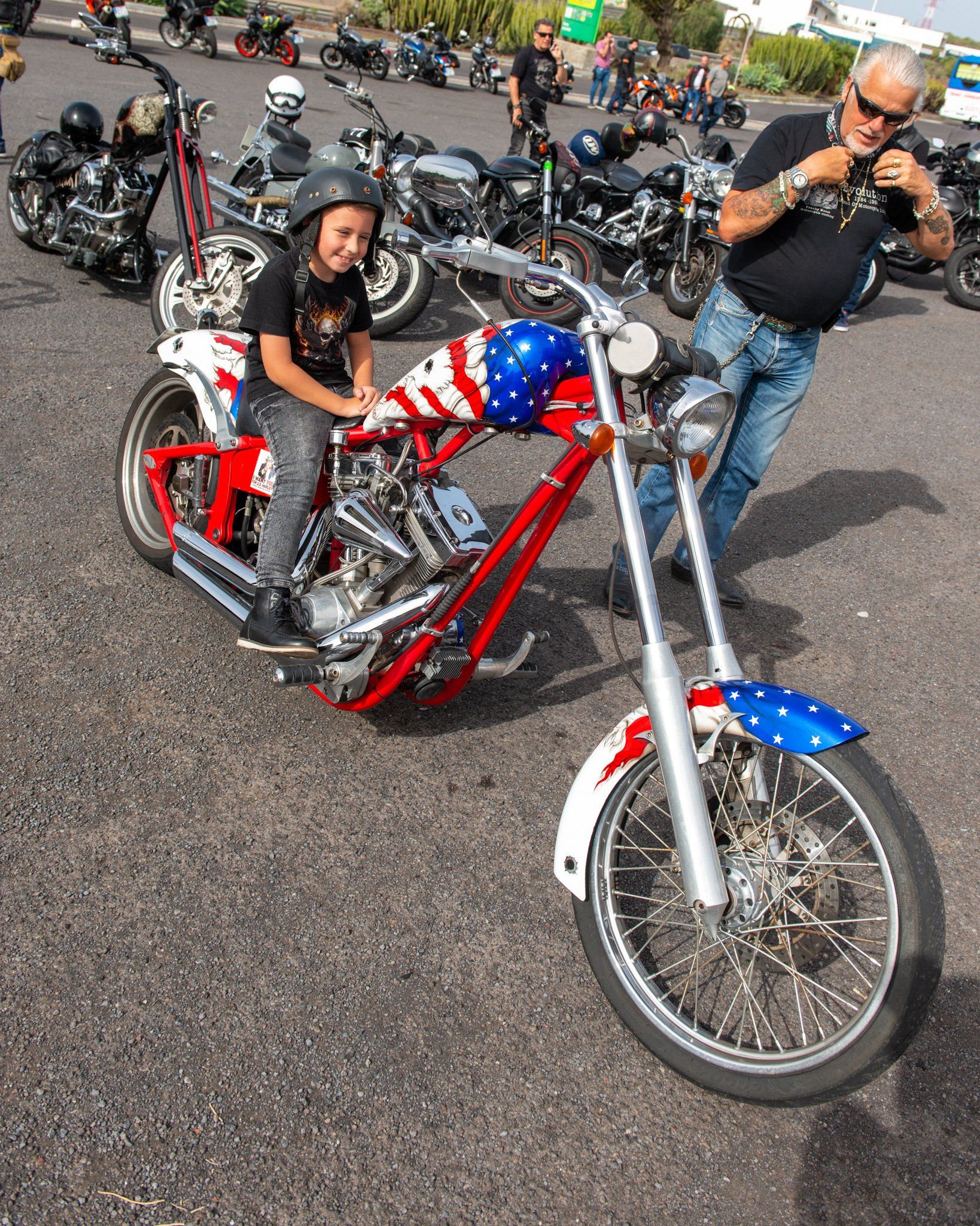 A boy is sitting on a red white and blue motorcycle