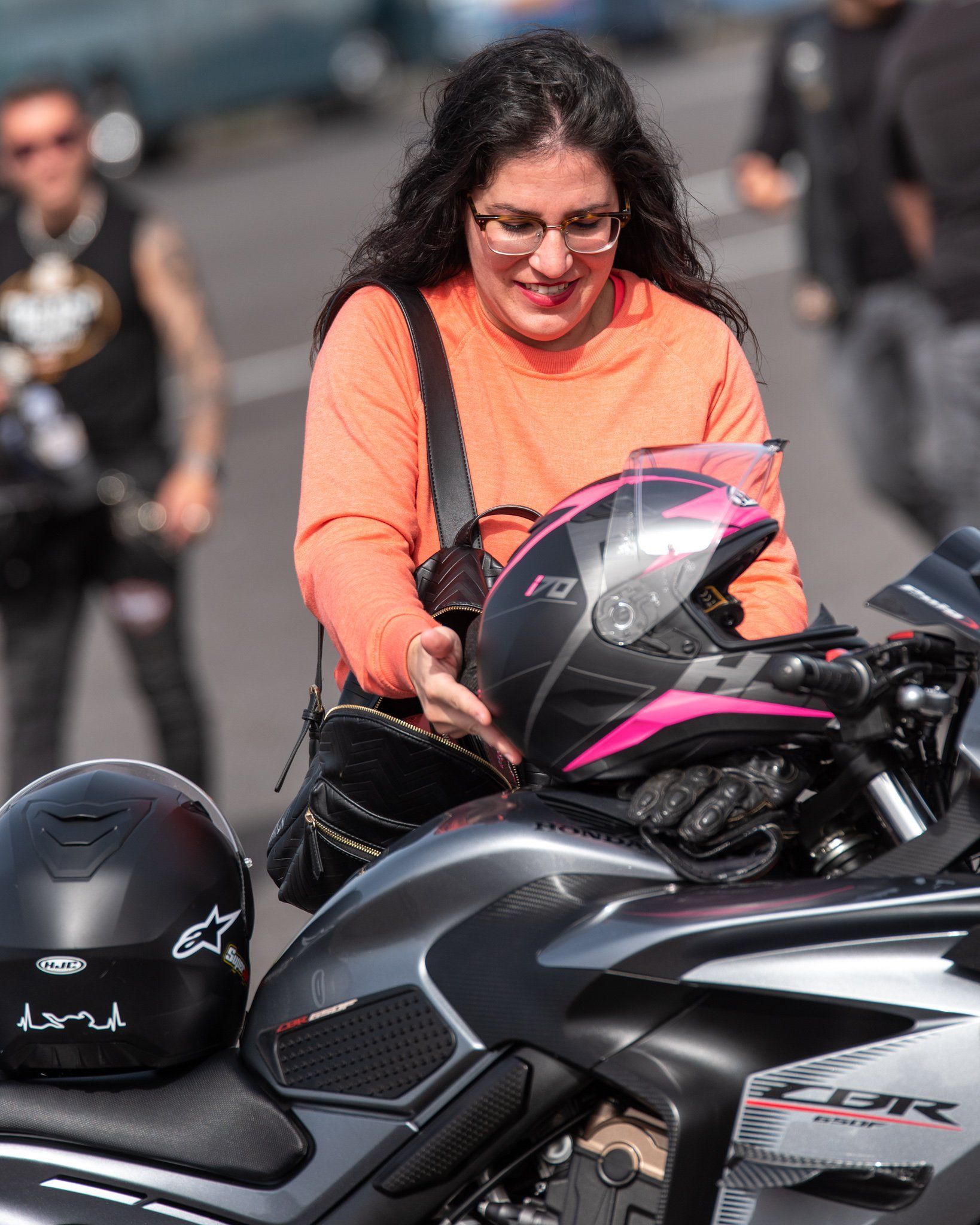 A woman is putting on a helmet on a motorcycle.