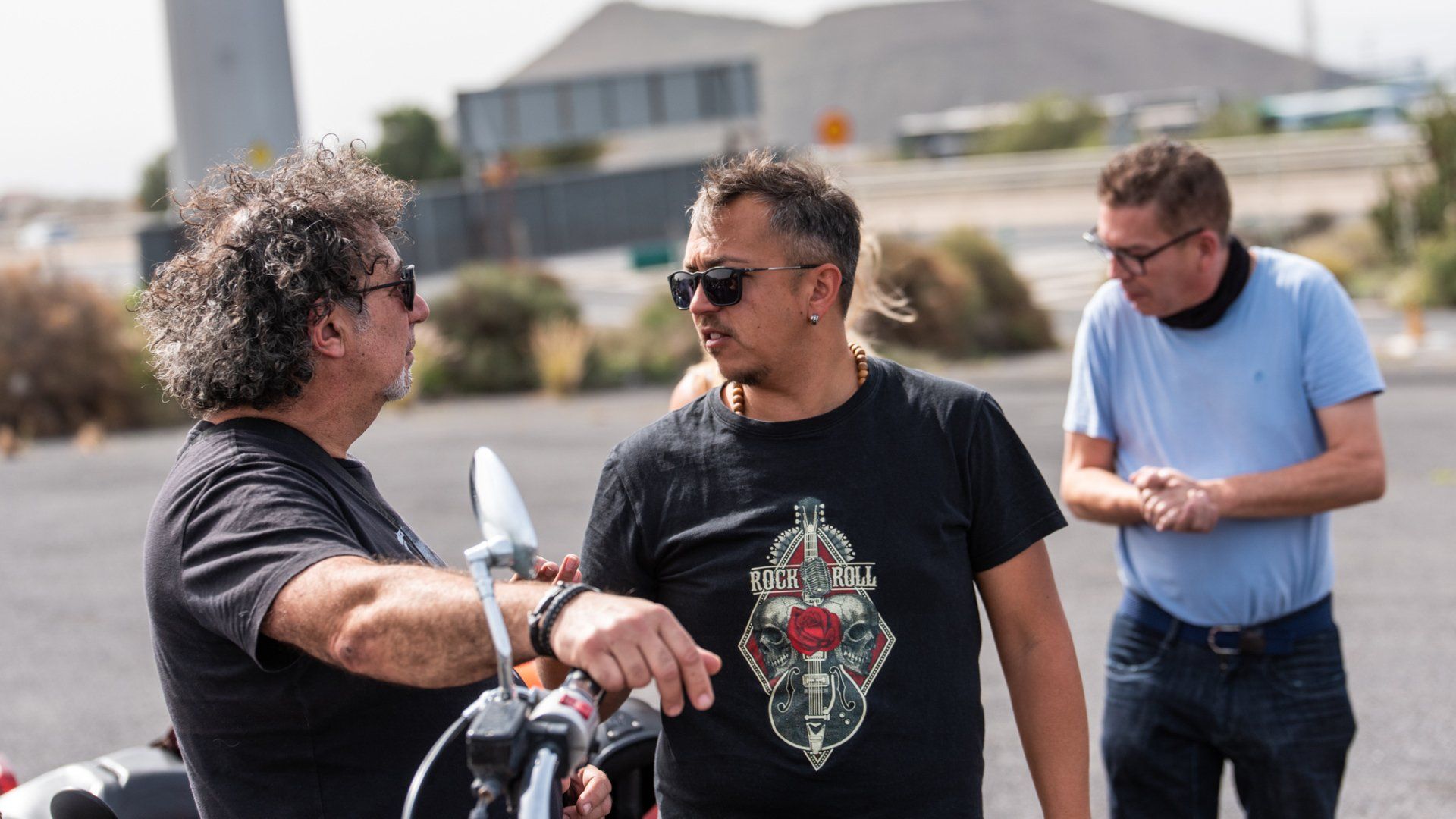 Three men are standing next to each other in a parking lot talking to each other.