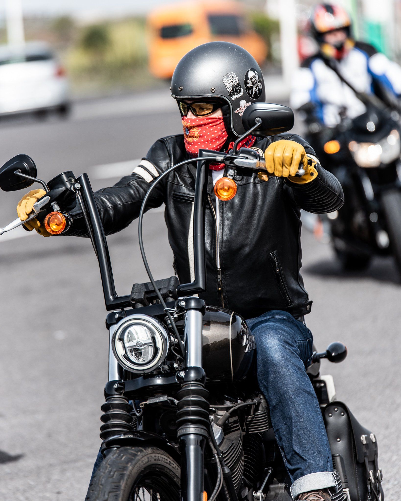 A man wearing a helmet and a bandana is riding a motorcycle down a street.