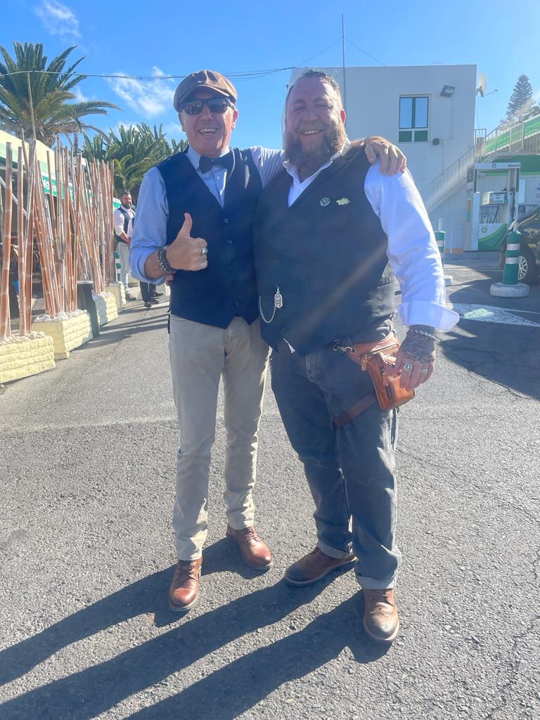 Two men are standing next to each other and one is giving a thumbs up.