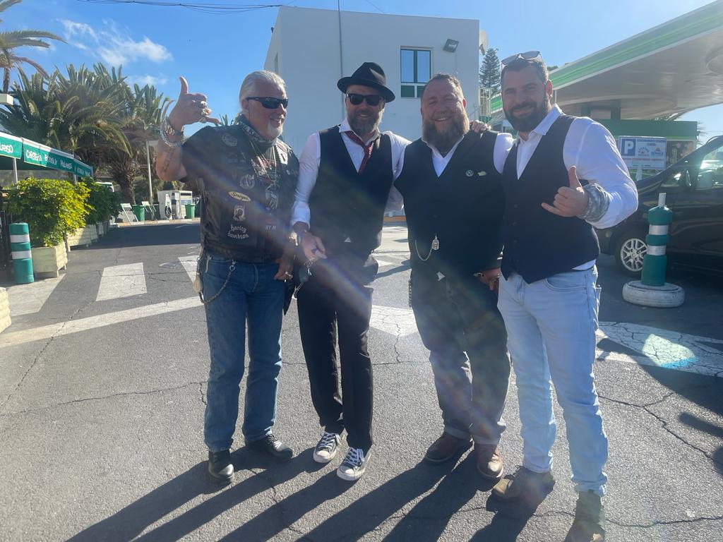 A group of men are posing for a picture in front of a gas station.