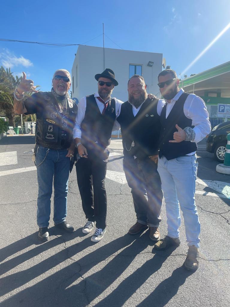 A group of men are posing for a picture in front of a gas station.