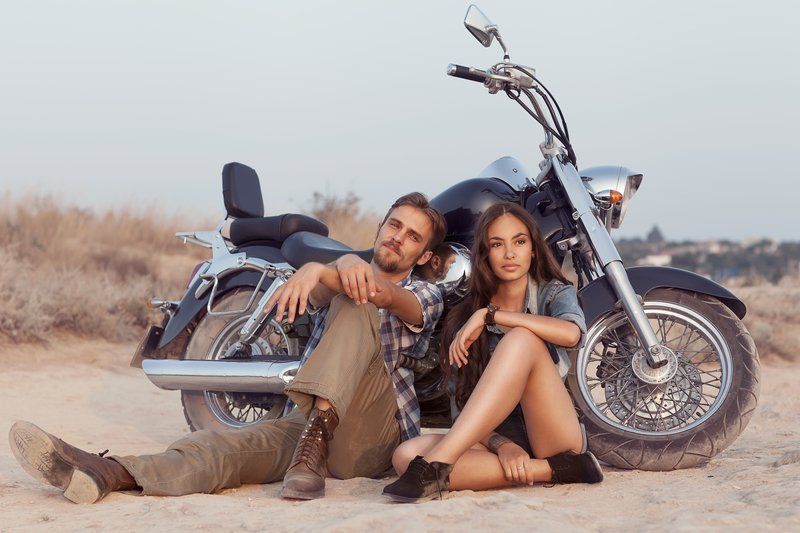 A man and a woman are sitting next to a motorcycle in the desert.