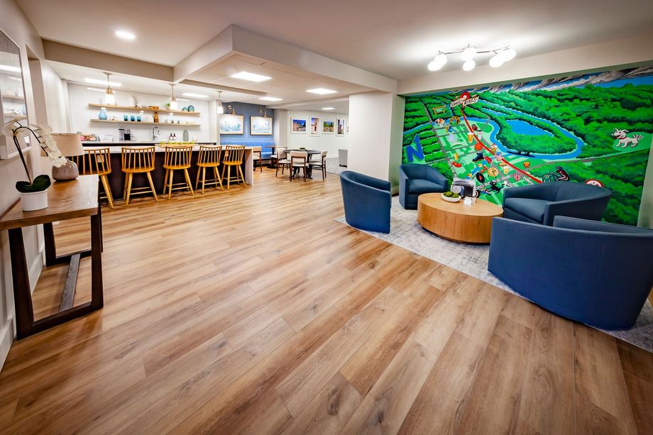 Clubhouse with wooden floors , chairs , tables and a mural on the wall.
