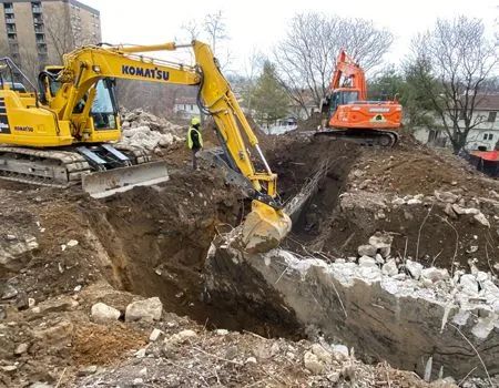 Two excavators digging into a pile of dirt and concrete; construction site.