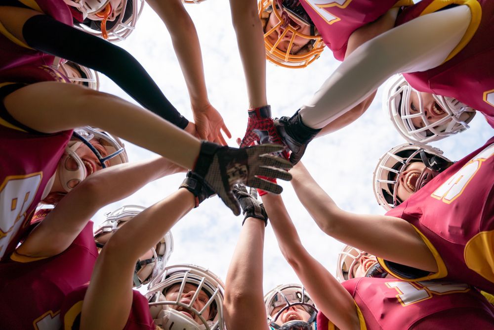 A group of football players are putting their hands together in a huddle.