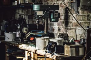 A drill is sitting on top of a wooden table in a garage.