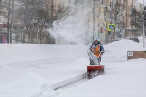 A man is blowing snow from a snow blower on a snowy street.