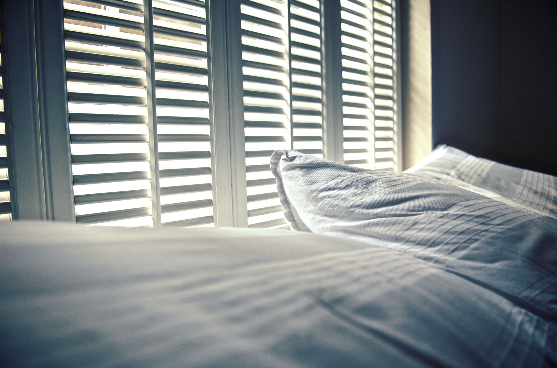 Bright bedroom view featuring white plantation shutters filtering natural morning sunlight.