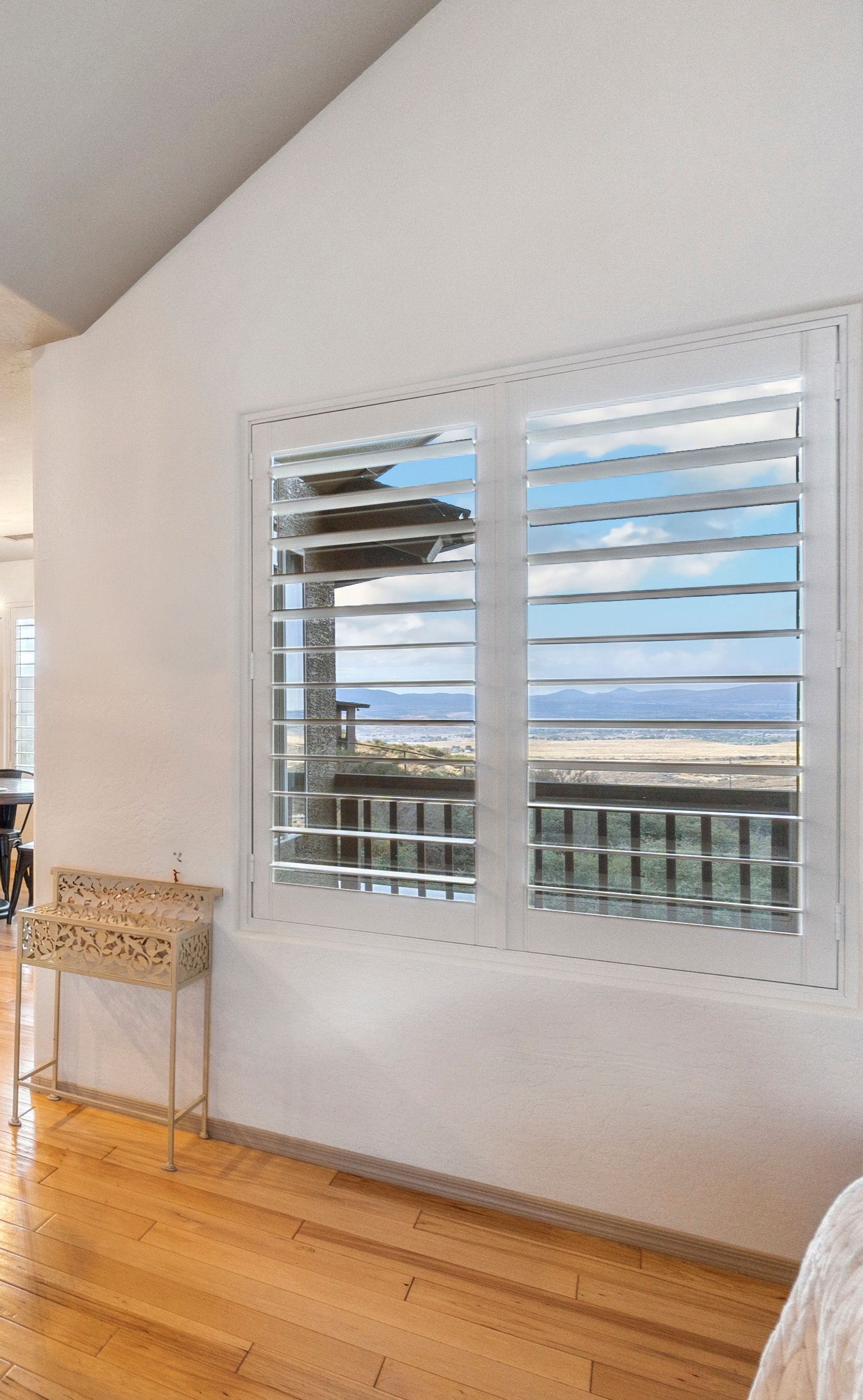 A room with wooden flooring, featuring a white wall and plantation shutters that overlook a scenic view outside