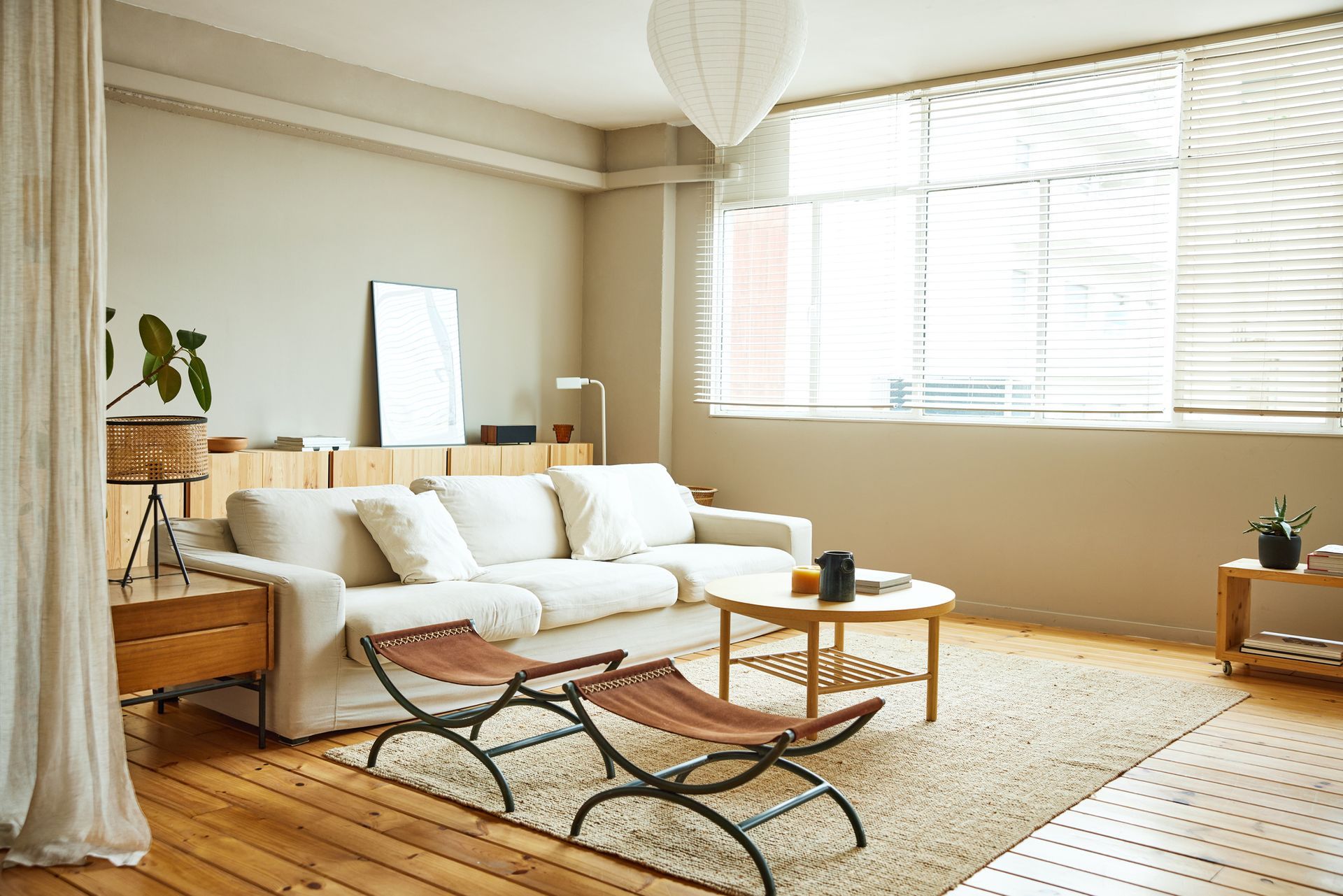 White horizontal blinds filter light into a cozy living room with modern furniture and decor.