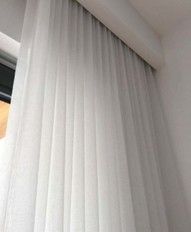 White pleated curtains hanging from a ceiling-mounted track in a modern interior room