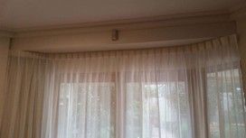 A large window with sheer white curtains hanging from a ceiling-mounted track in a bright interior