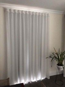 White sheer curtains hanging from a rod in a bright room with a potted plant on a black metal stand