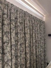 Beige curtains with a floral pattern hanging from a ceiling-mounted track in a room