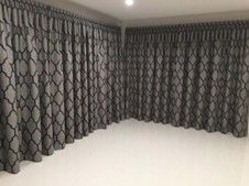 Empty room with two walls of windows covered by grey patterned curtains and white ceiling moulding