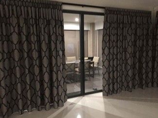 A sliding glass door with grey patterned curtains partially open, revealing a patio with chairs