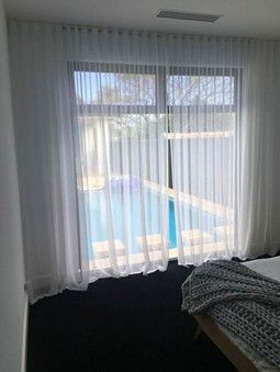 A bedroom window with sheer white curtains overlooking a swimming pool