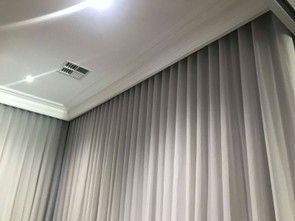 Grey pleated curtains hanging from a ceiling-mounted track in a modern room with recessed lighting