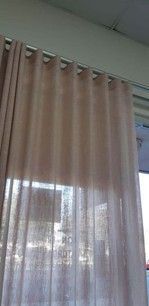 A light pink sheer curtain with soft pleats hanging from a ceiling-mounted track