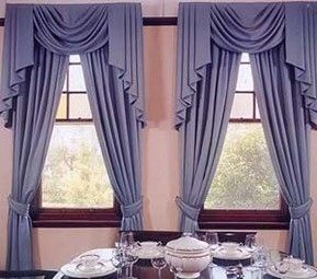 Dining room windows with blue draped curtains and valances framing a wooden table set for a meal