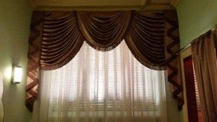 A window with sheer white curtains and ornate brown drapes in a mint green room