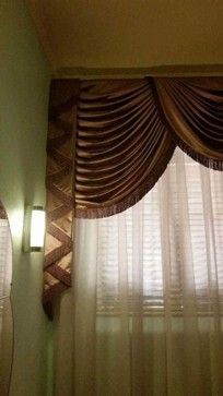 A brown draped valance with sheer white curtains and a wall light on a mint green wall